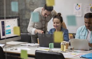 Grupo de jovens profissionais trabalhando em equipe em um escritório moderno com computadores, gráficos e anotações, representando o ambiente colaborativo e inovador das startups brasileiras