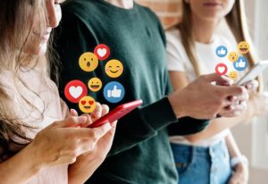 Três pessoas utilizando seus celulares com emojis flutuando ao redor das telas, representando expressões como curtidas, risadas e corações, simbolizando a influência dos emojis na comunicação digital.
