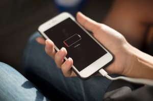 Pessoa segurando um smartphone com tela mostrando ícone de bateria fraca enquanto começa a carregar o celular com cabo conectado.